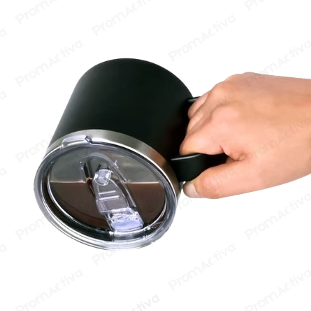 Mano sosteniendo jarro térmico negro mate de acero inoxidable con asa, mostrando la tapa deslizable antiderrame.